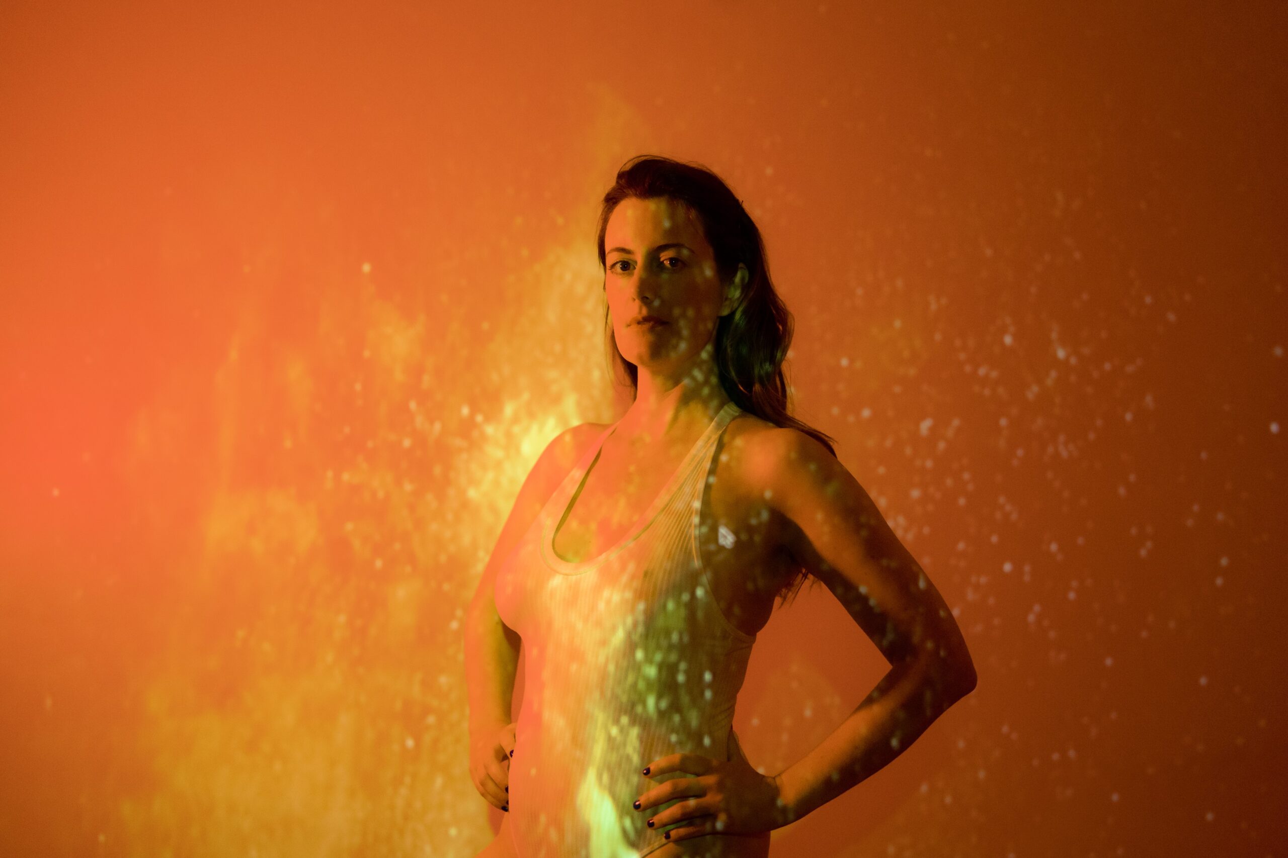 A radiating Skylar in a sequined sleeveless dress against an orange background