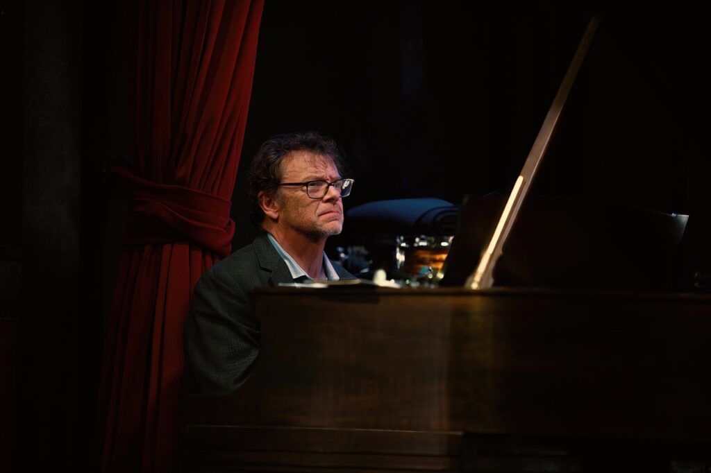 Greg Bell on stage behind a piano