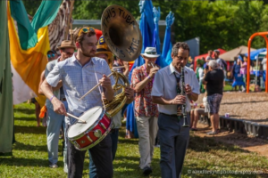 Festive scene with people marching and playing horns and a drum. 