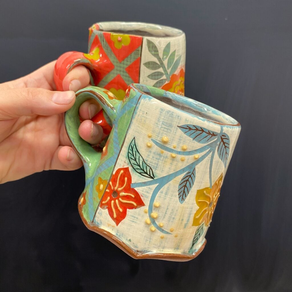 someone holding two handmade mugs